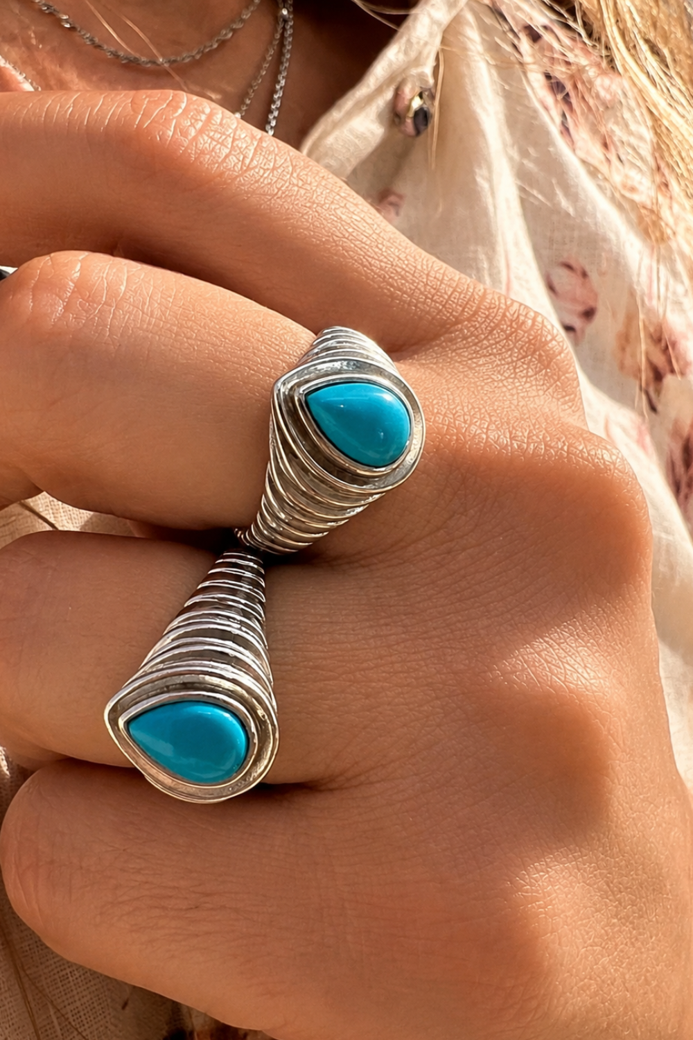 Two sculptural silver turquoise rings stacked on the hand by Galleria Armadoro in warm summer sunlight.