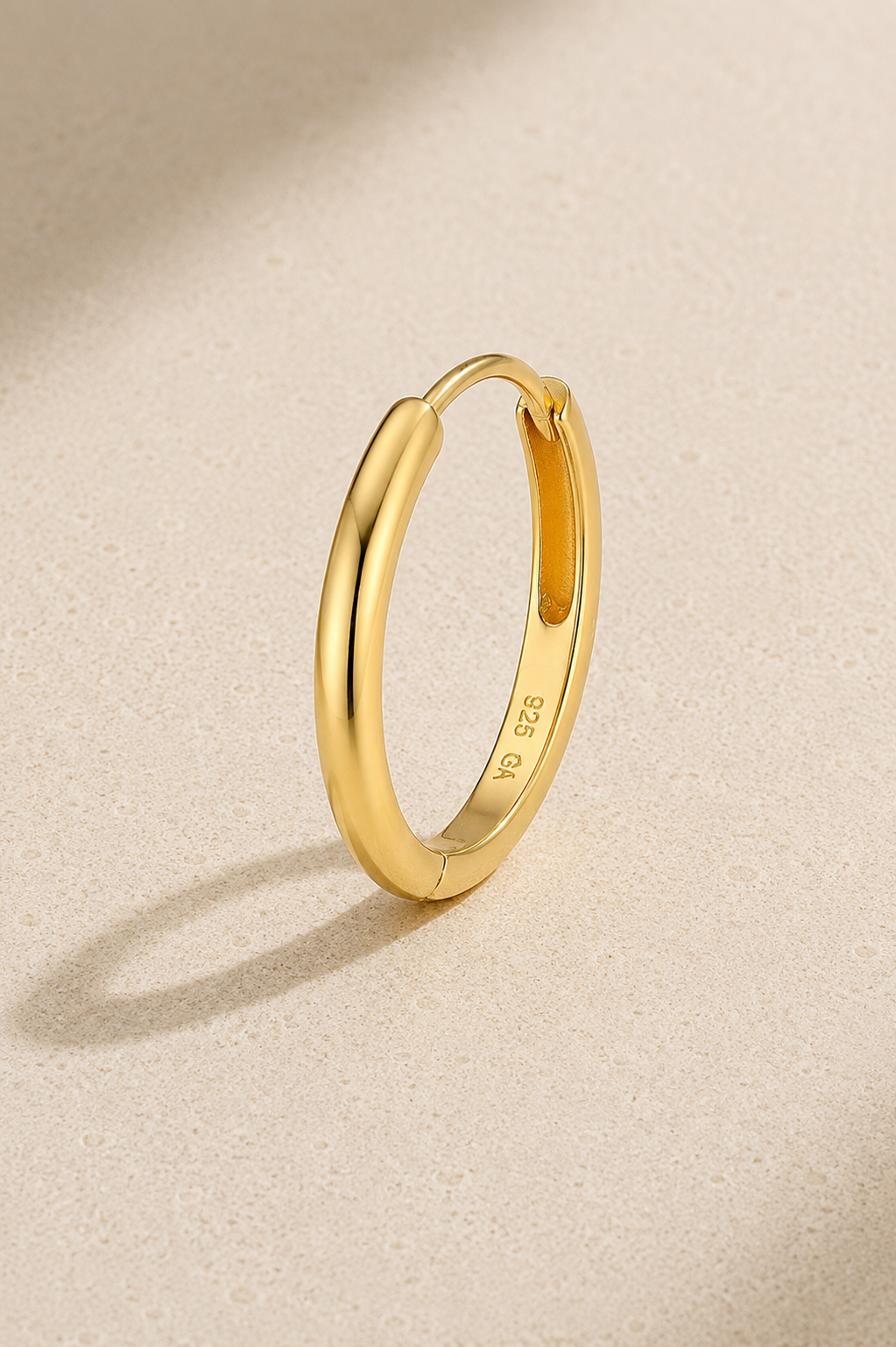 12.5mm gold huggie earring in 925 sterling silver with thick 24ct gold plating on beige studio background