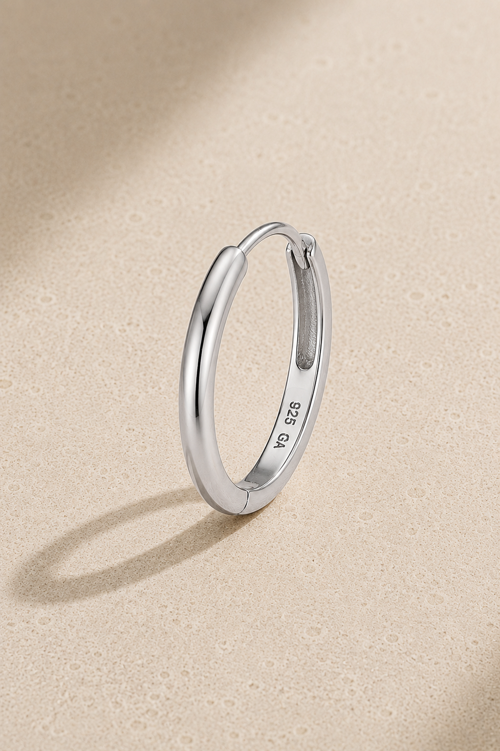 12.5mm silver huggie earring in 925 sterling silver with white rhodium plating on beige studio background
