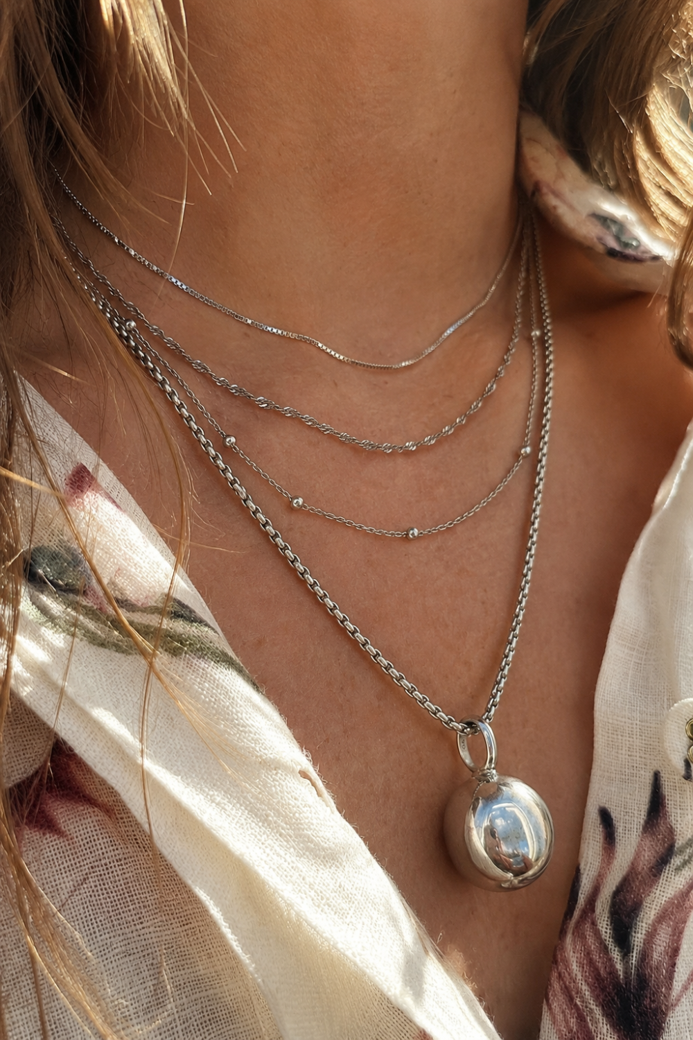 Layered silver necklaces by Galleria Armadoro styled with fine chains, textured silver chains and a sculptural silver pendant.