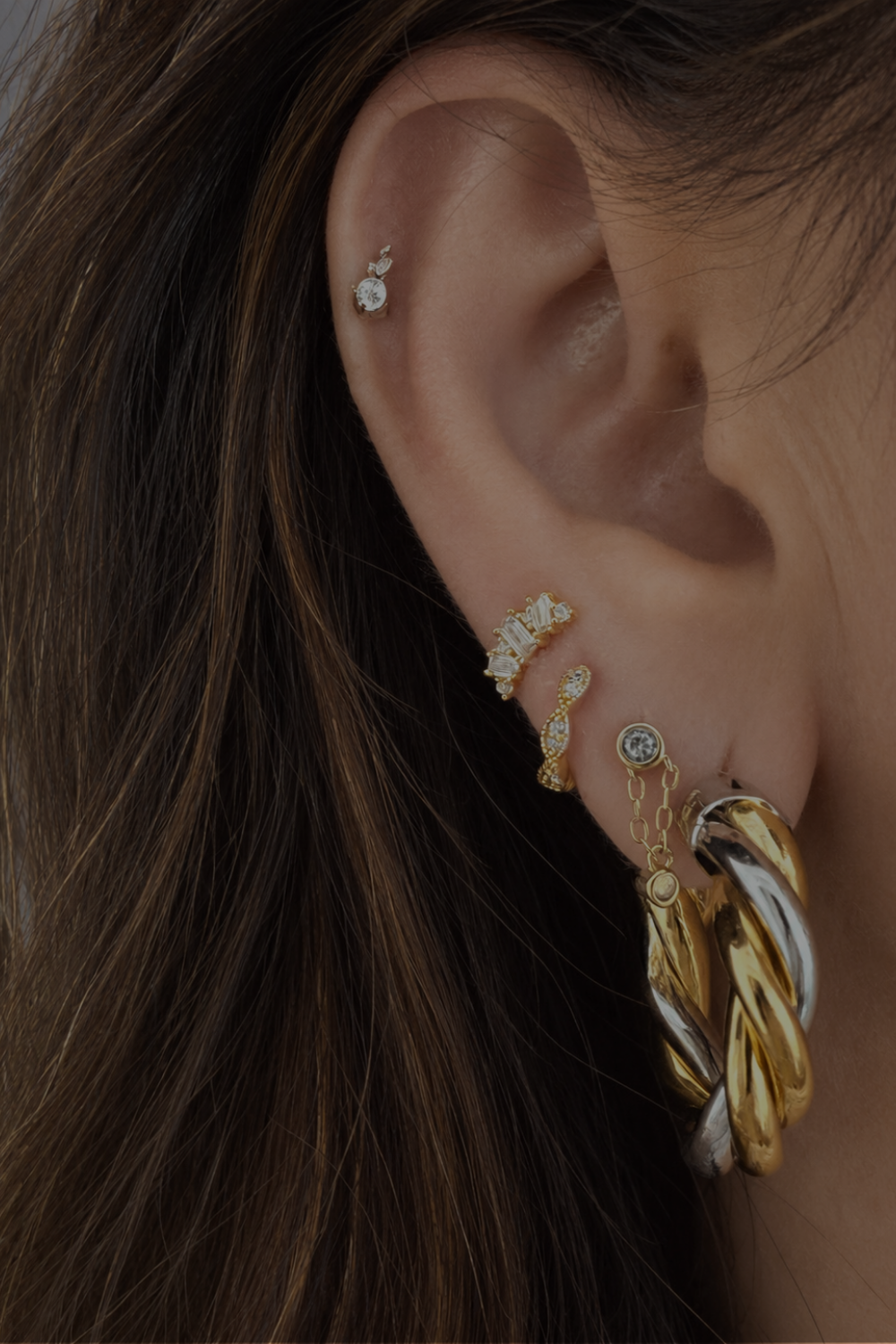 Dimitra’s mixed-metal ear look by Galleria Armadoro featuring 3 cm Two-Tone Tina Hoops styled with delicate huggies and stud earrings.