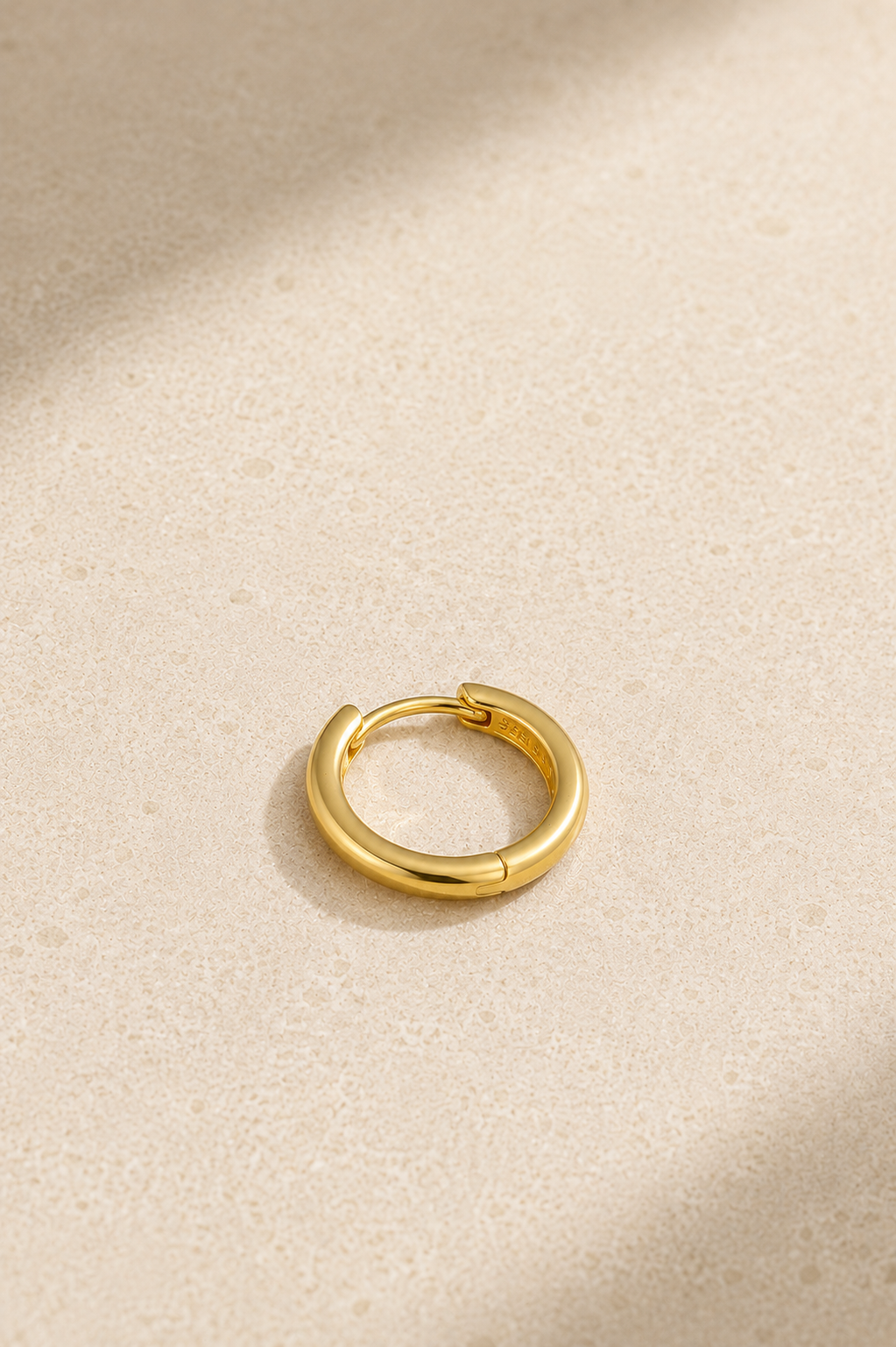 Small gold huggie hoop earring lying flat, ideal for everyday ear stacks and cartilage piercings