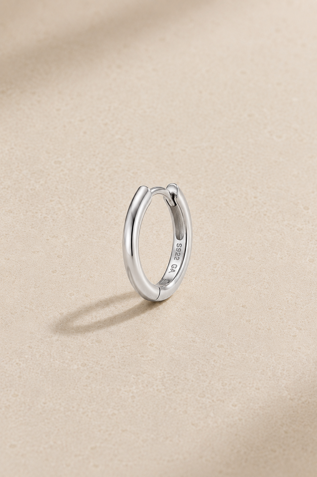 8.5mm silver huggie earring in 925 sterling silver with white rhodium plating standing upright on beige studio background