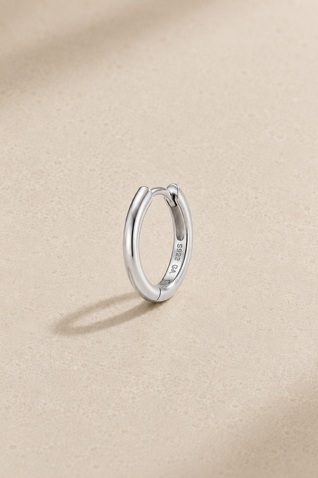 8.5mm silver huggie earring in 925 sterling silver with white rhodium plating standing upright on beige studio background