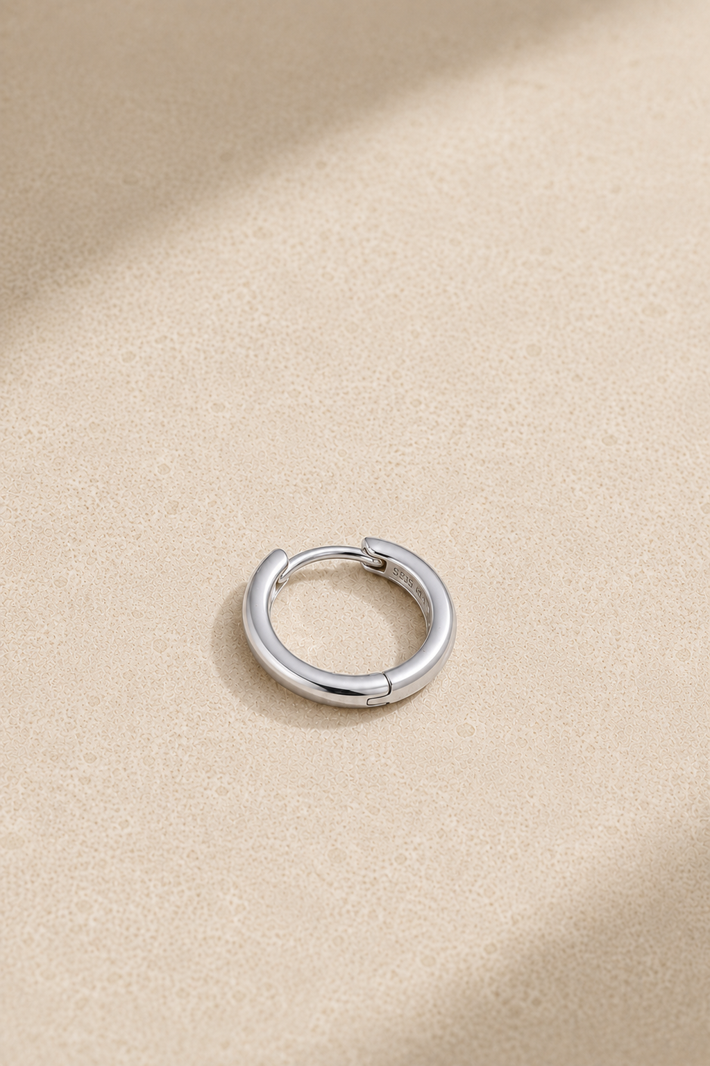 Small silver huggie hoop earring lying flat, ideal for everyday ear stacks and cartilage piercings
