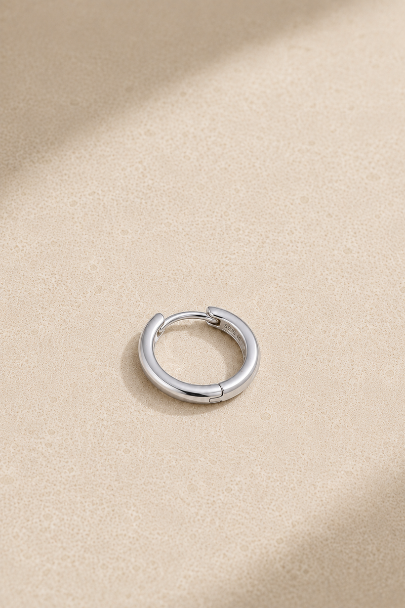 Small silver huggie hoop earring lying flat, ideal for everyday ear stacks and cartilage piercings