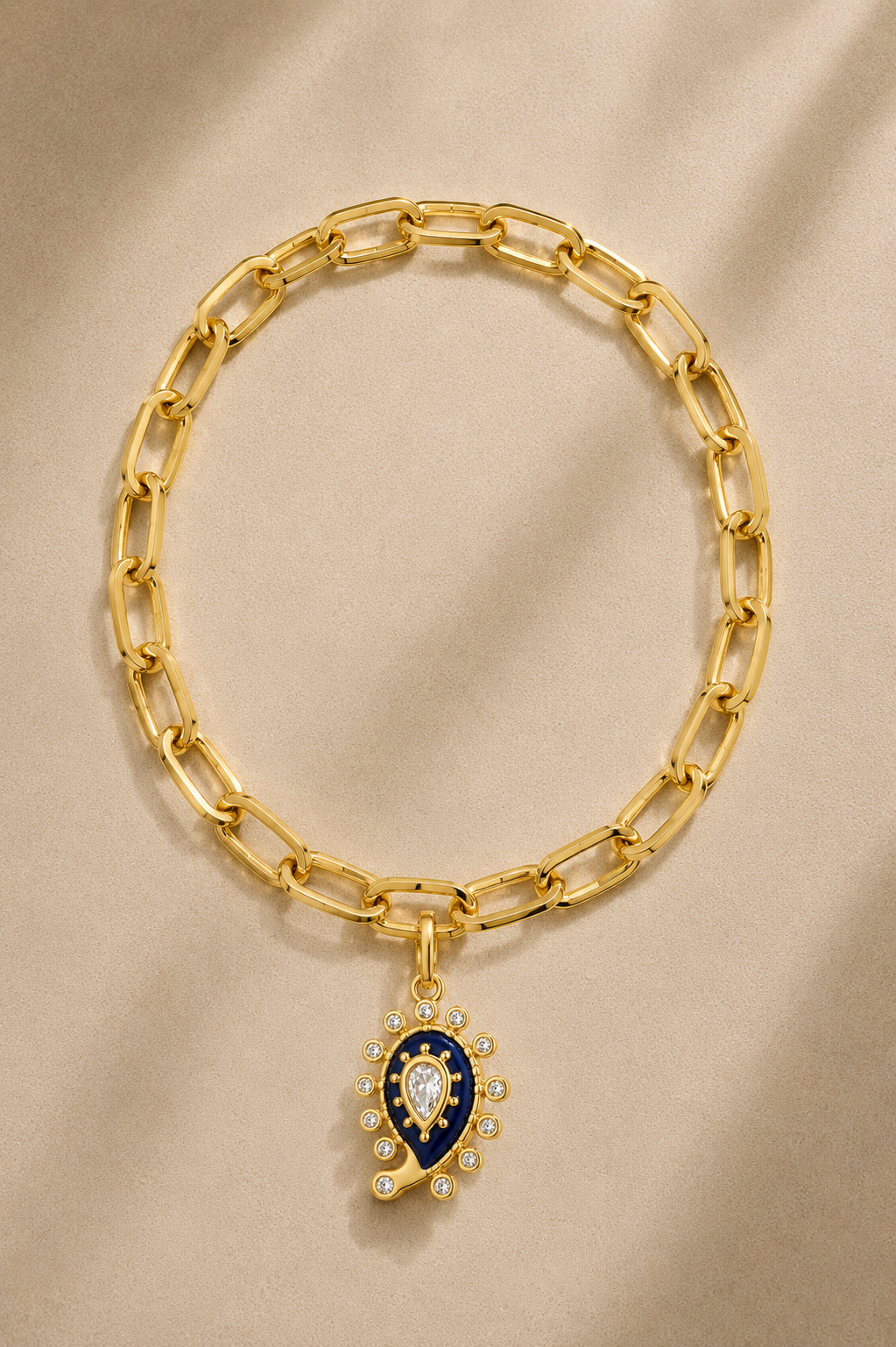 Cara chunky gold bracelet with lapis paisley evil eye charm on beige background