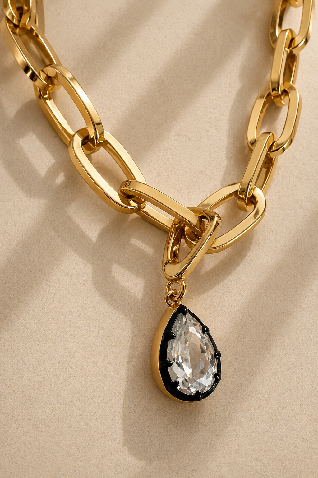 Cara chunky gold paperclip chain necklace with Vittoria black rhodium crystal charm on beige background
