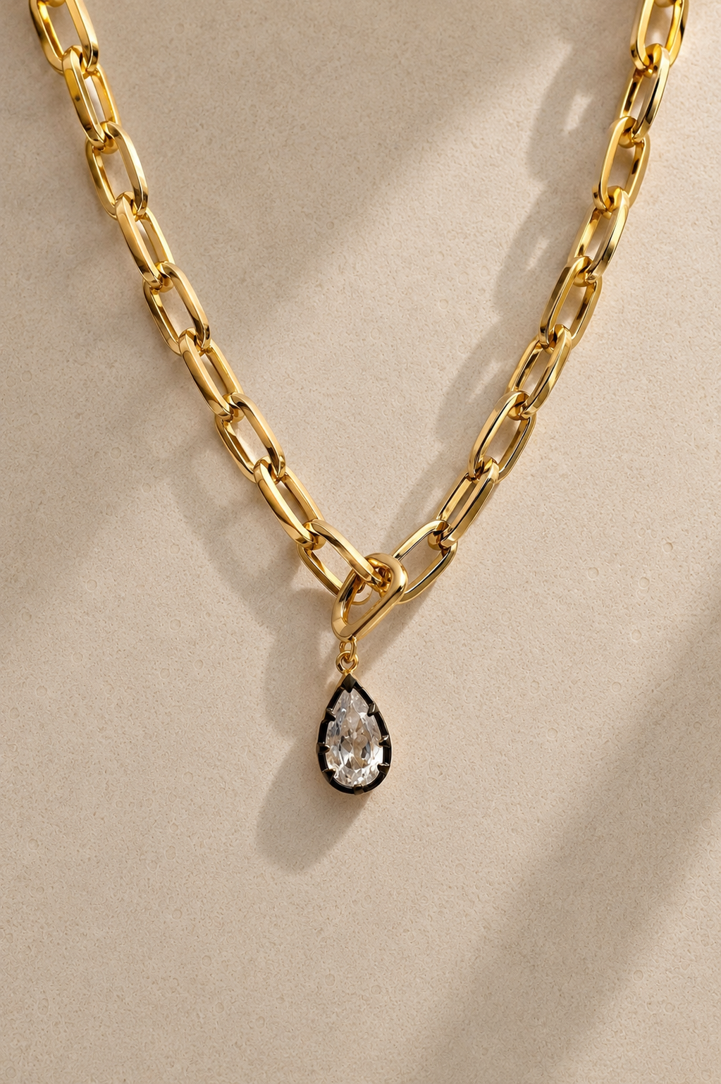 Cara chunky gold paperclip chain necklace with Vittoria black rhodium crystal charm on beige background