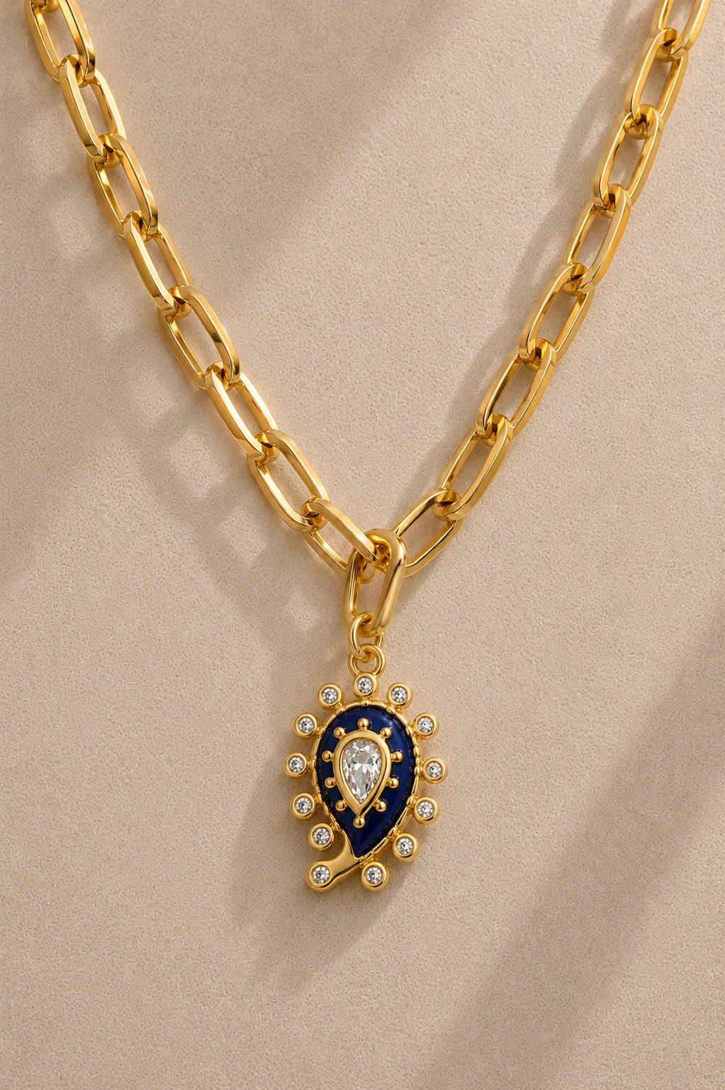 Cara chunky gold paperclip chain necklace with lapis paisley evil eye charm on beige background