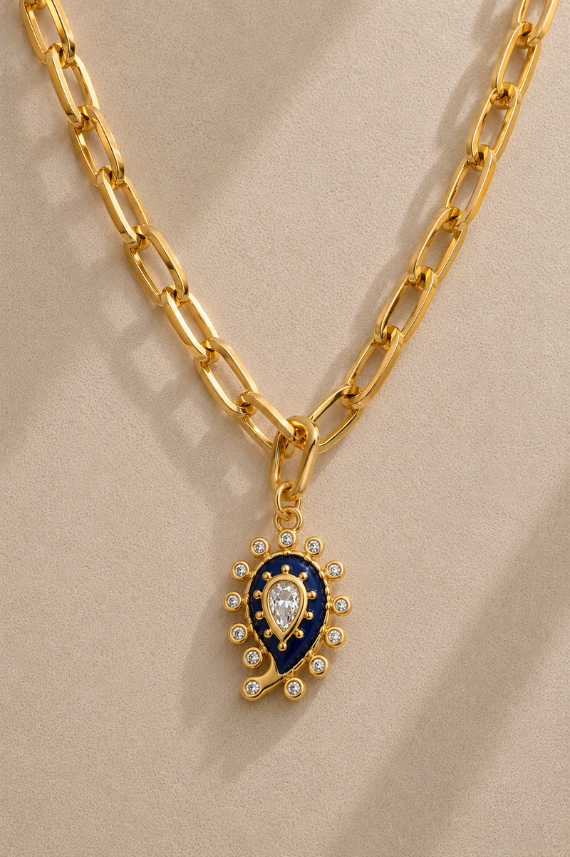 Cara chunky gold paperclip chain necklace with lapis paisley evil eye charm on beige background