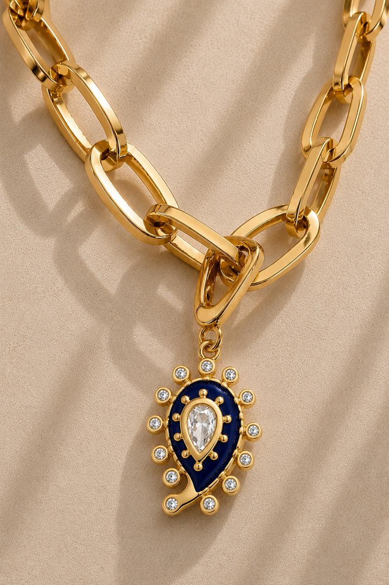 Close-up of oversized gold paperclip chain with blue paisley evil eye charm and crystal details