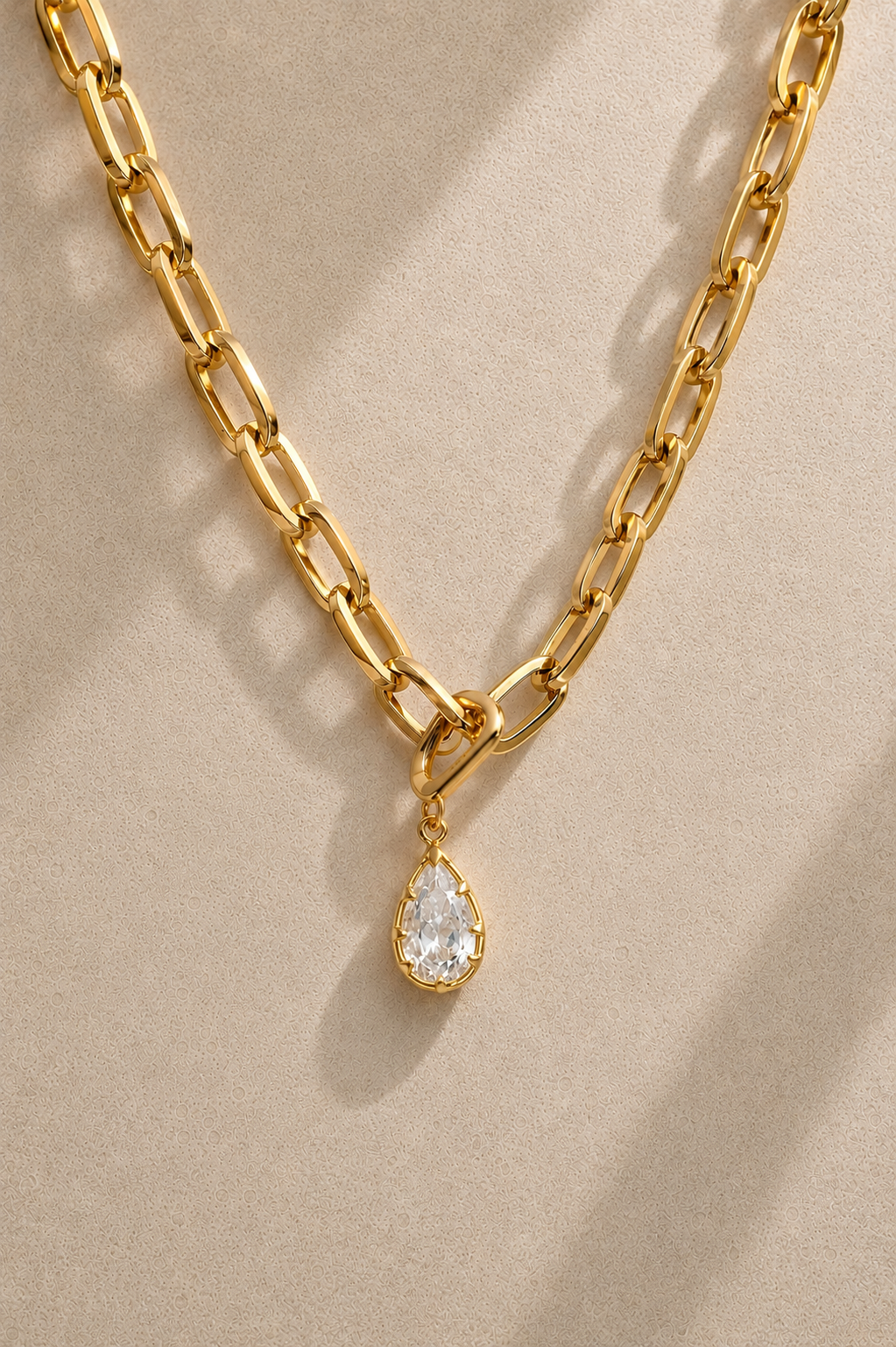 Cara chunky gold paperclip chain necklace with Vittoria gold crystal charm on beige background