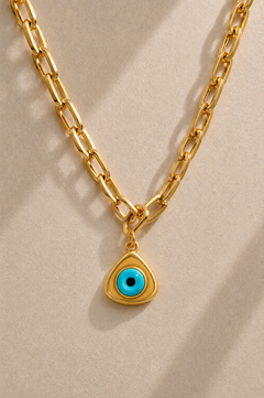 Cara chunky gold paperclip chain necklace with triangle evil eye charm on beige background