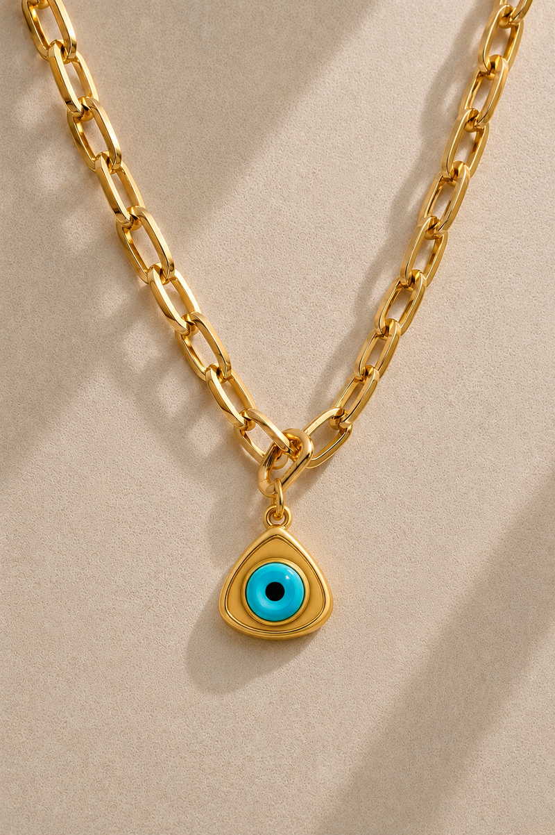 Cara chunky gold paperclip chain necklace with triangle evil eye charm on beige background