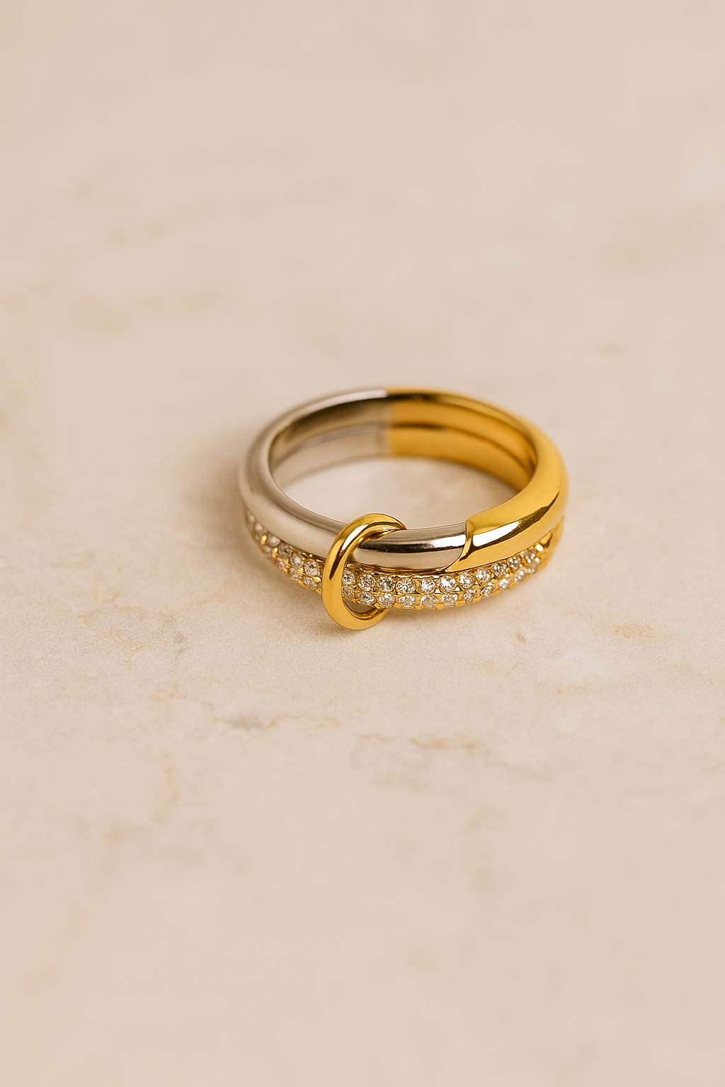 Close-up of Nora Speira ring on marble surface showing half-gold half-silver band and pavé detail.