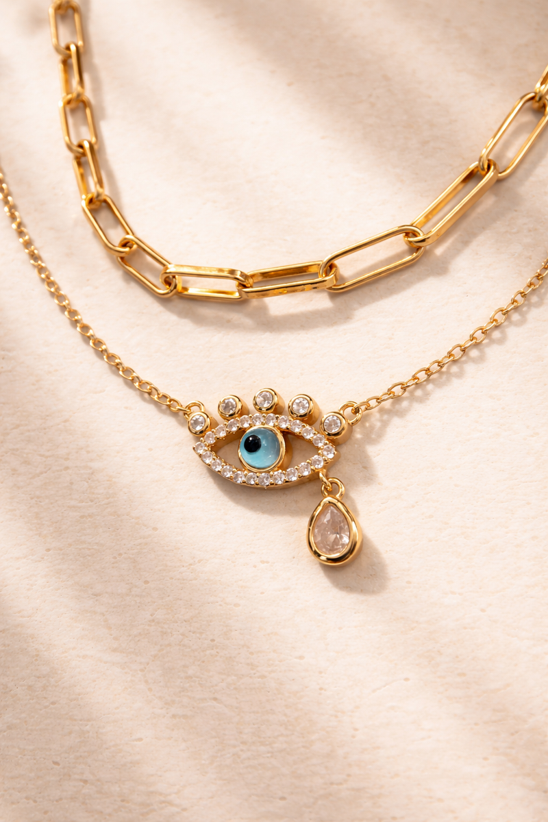 Large link gold chain and evil eye necklace styled together on minimal background