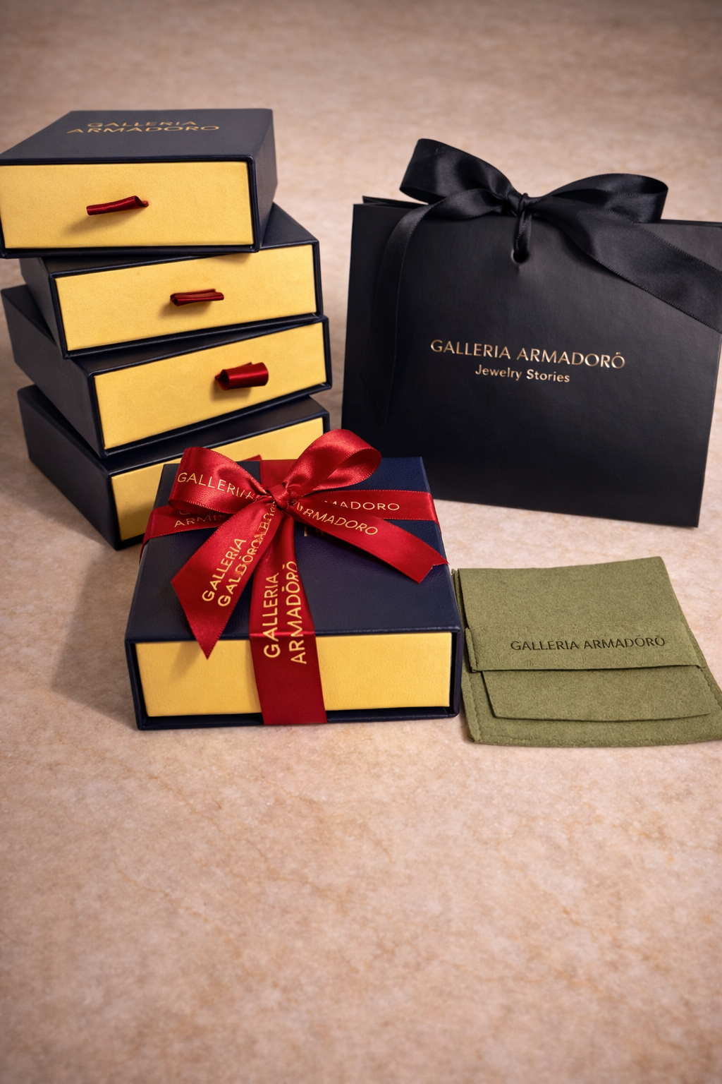 Luxury jewellery packaging set including navy blue drawer boxes with gold logo, red ribbon gift box, black shopping bag with “Jewelry Stories” tagline, and olive suede pouch displayed on beige marble background.