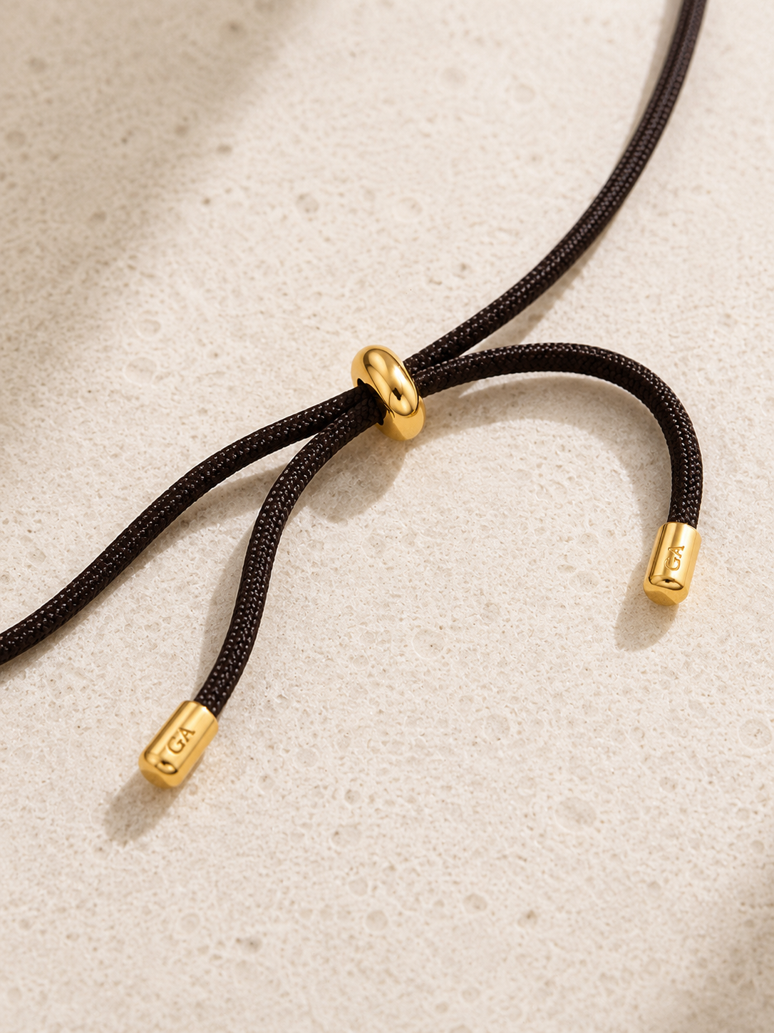 Close-up of adjustable gold-plated slider detail on black cord necklace