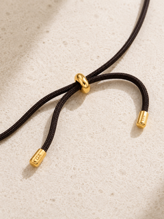 Close-up of adjustable gold-plated slider detail on black cord necklace