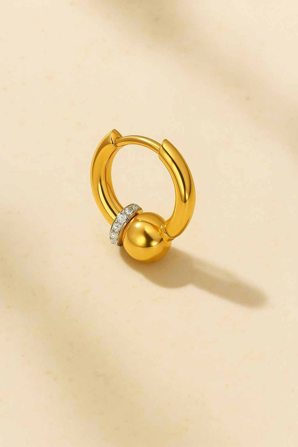 Gold Kora bead huggie earring on marble with soft directional lighting