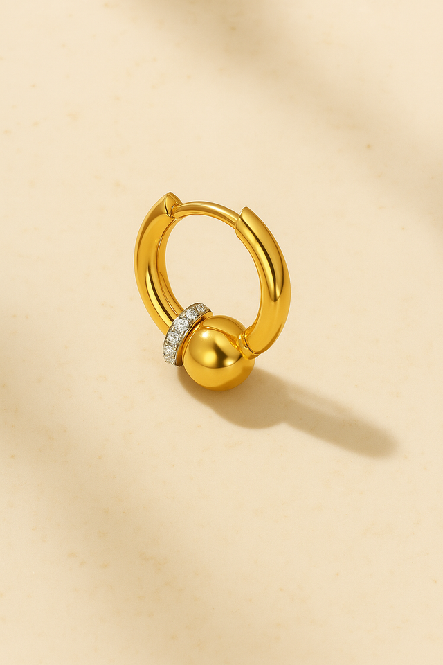 Gold Kora bead huggie earring on marble with soft directional lighting