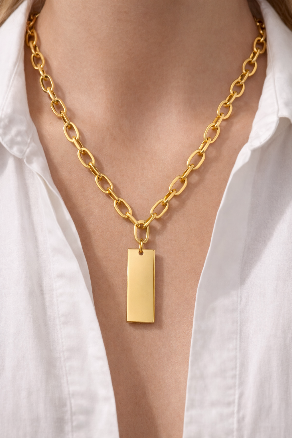 Gold dog tag necklace styling on model wearing open white cropped shirt, close-up”