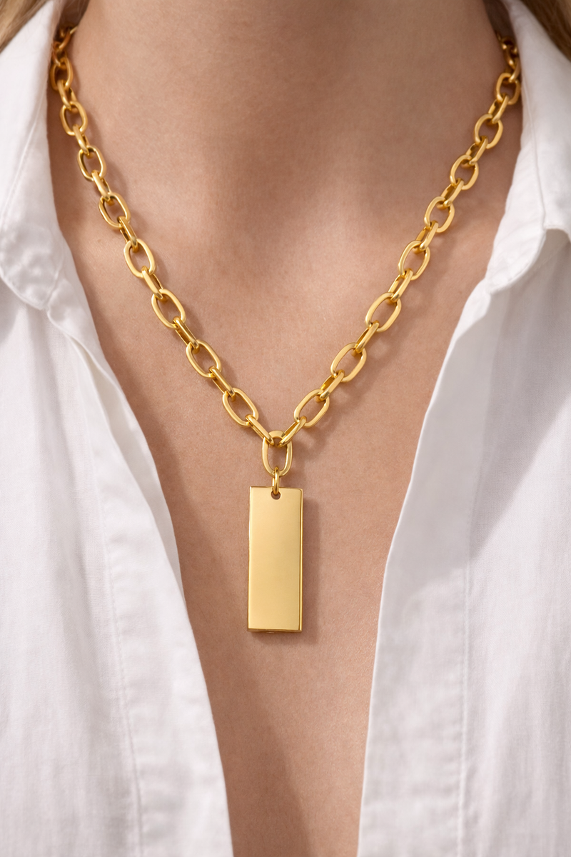Gold dog tag necklace styling on model wearing open white cropped shirt, close-up”