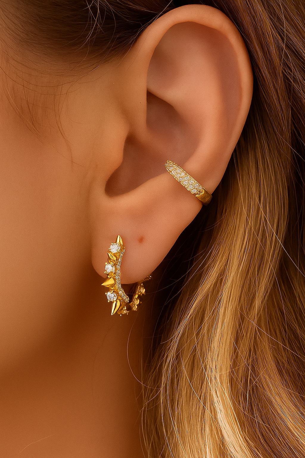 Gold pavé ear cuff worn above hoop earring, close-up on mid-ear placement.