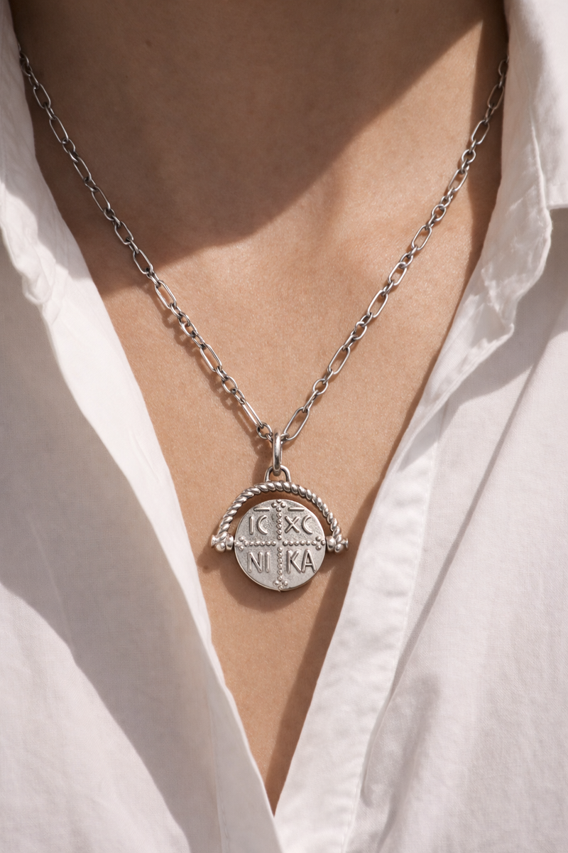 Konstantinato coin pendant necklace on slim sterling silver chain worn over a crisp white shirt, strong studio shadows