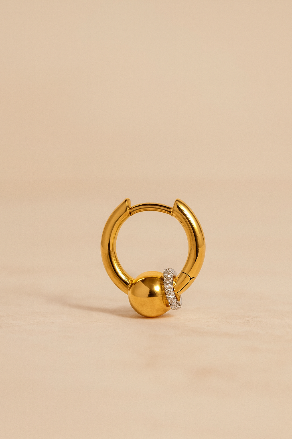 Gold Kora bead huggie earring on marble with soft directional lighting