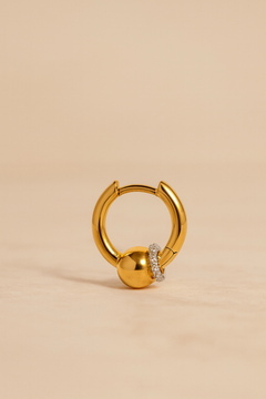 Gold Kora bead huggie earring on marble with soft directional lighting