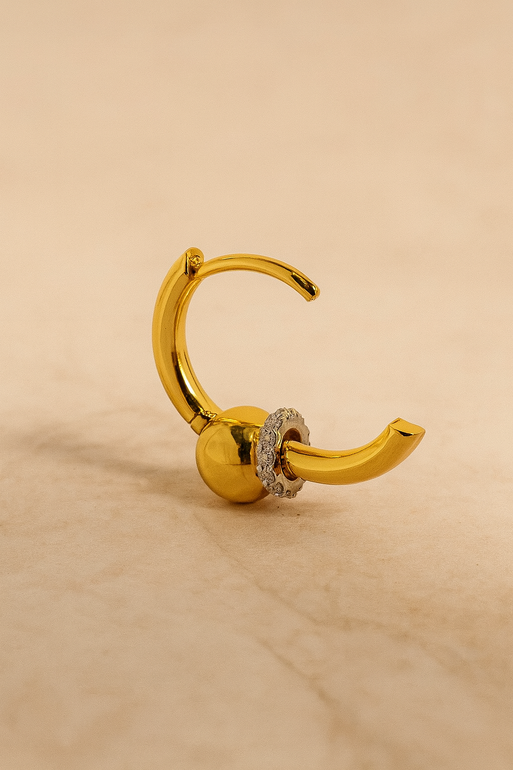 Kora gold huggie casting soft shadow on cream marble background