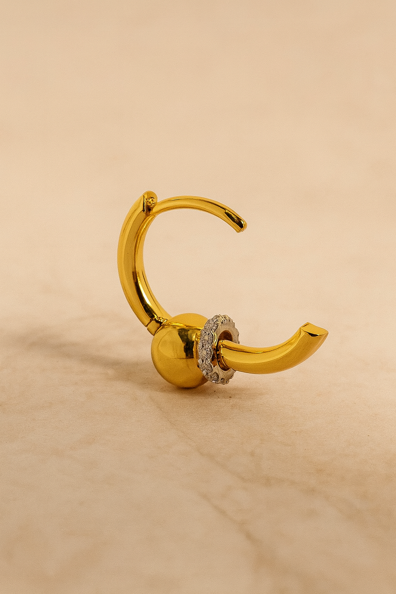 Kora gold huggie casting soft shadow on cream marble background