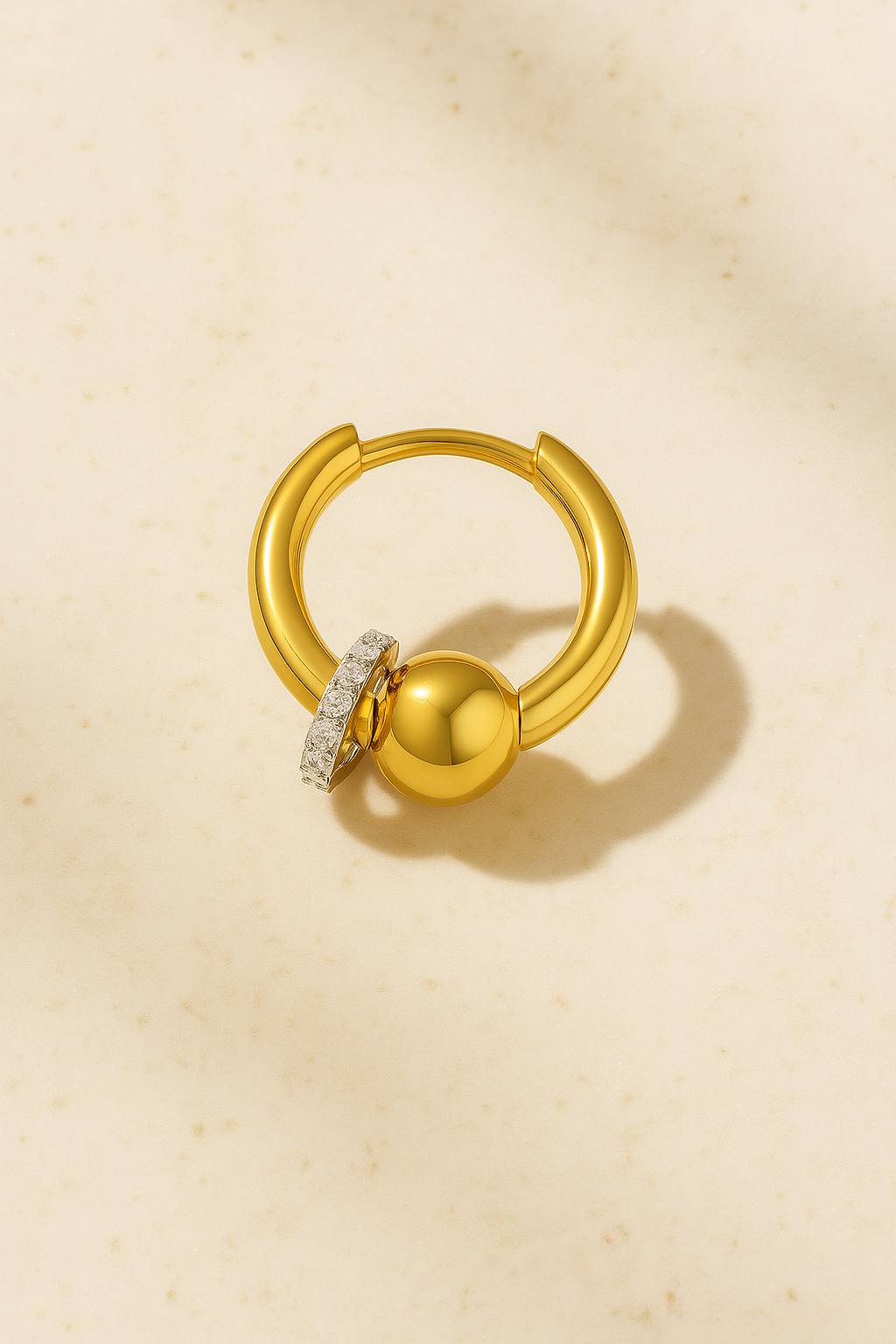 Kora gold piercing bead huggie on matte beige marble background