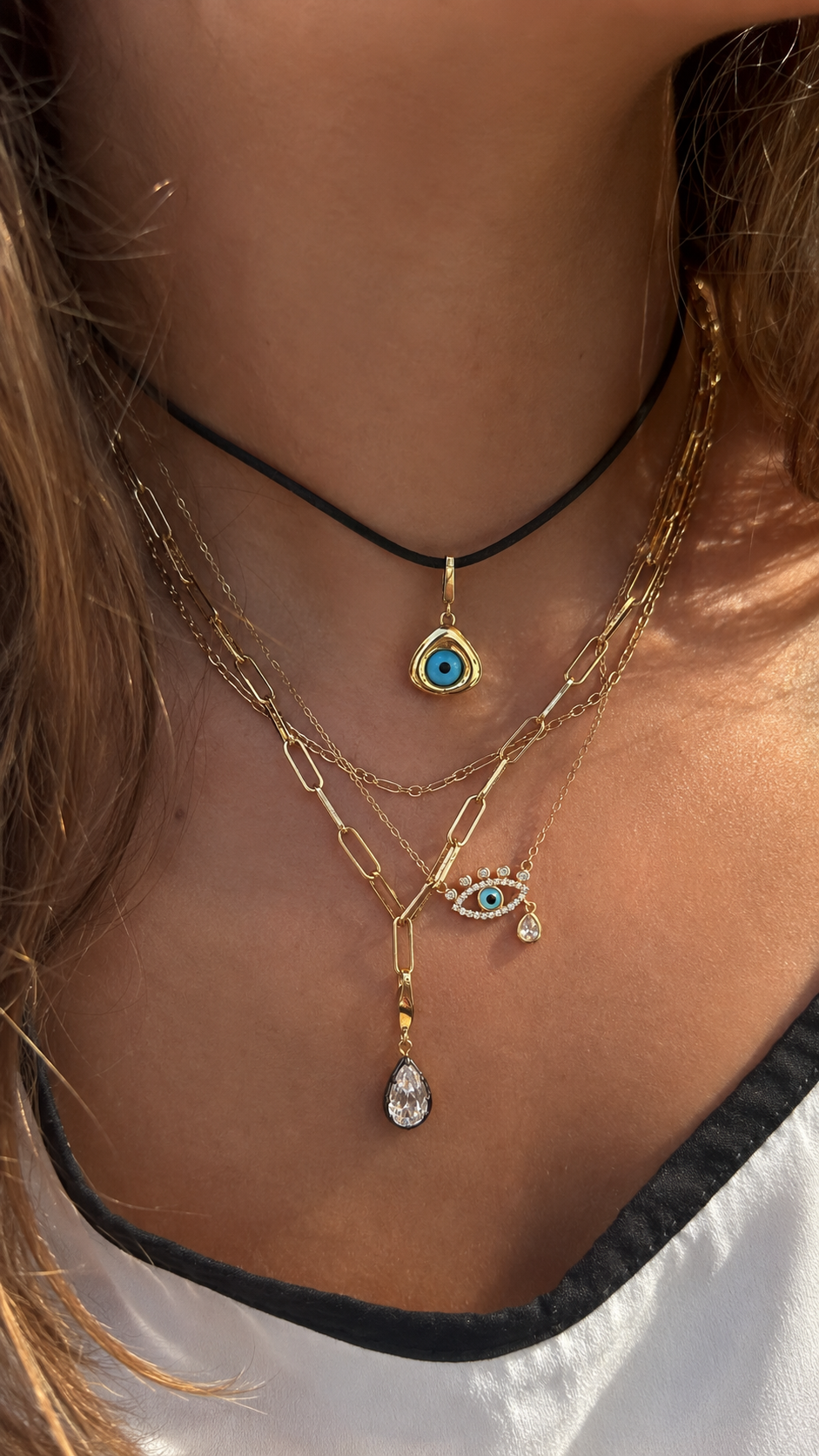 Layered gold necklaces styled by Galleria Armadoro with an evil eye pendant, black cord, paperclip chains and teardrop charms.