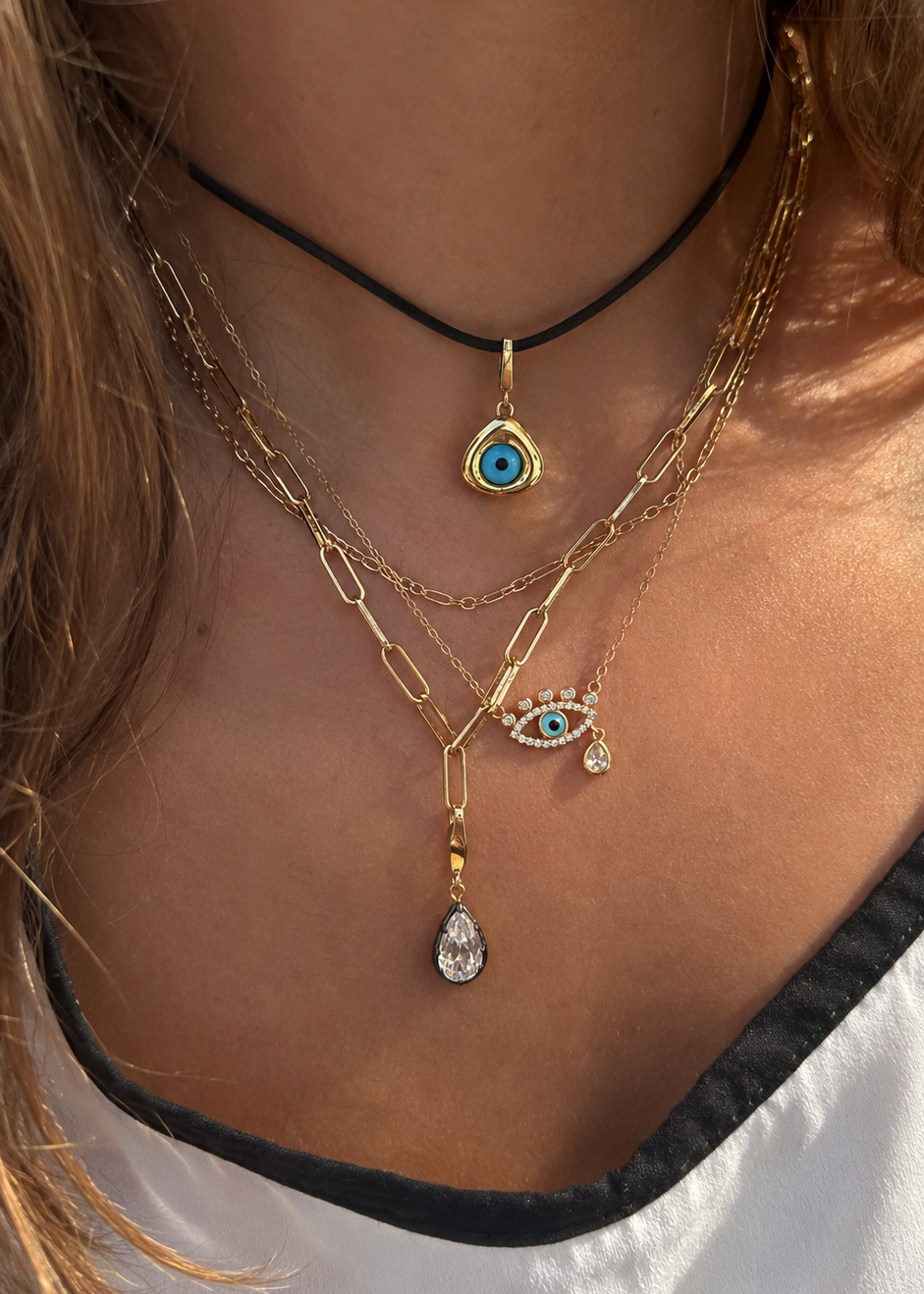 Layered gold necklaces styled by Galleria Armadoro with an evil eye pendant, black cord, paperclip chains and teardrop charms.