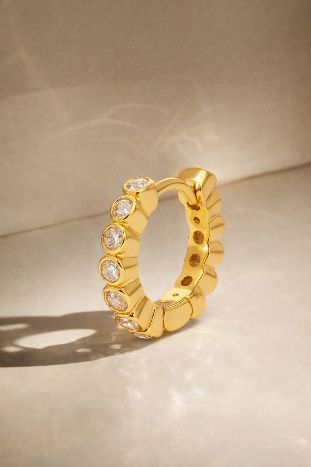 Gold hoop earring with embedded stones on a beige background