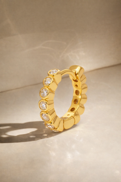 Gold hoop earring with embedded stones on a beige background