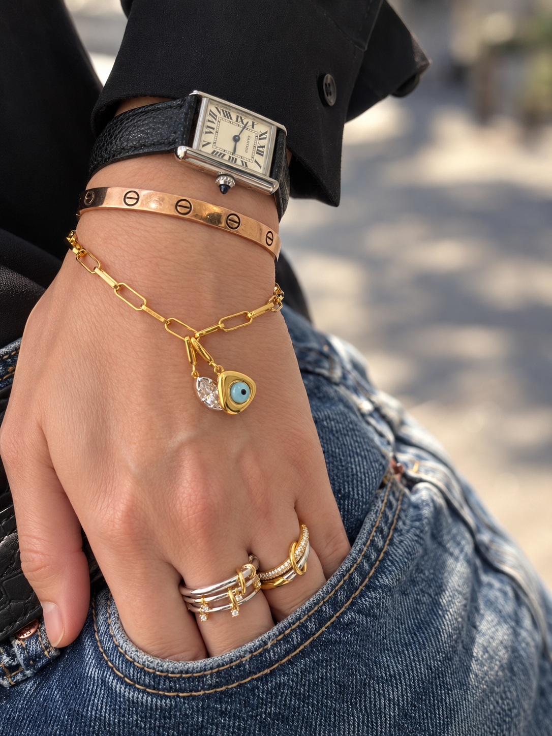 Gold charm bracelet by Galleria Armadoro styled with a marquise crystal charm, evil eye charm and mixed-metal ring stack.