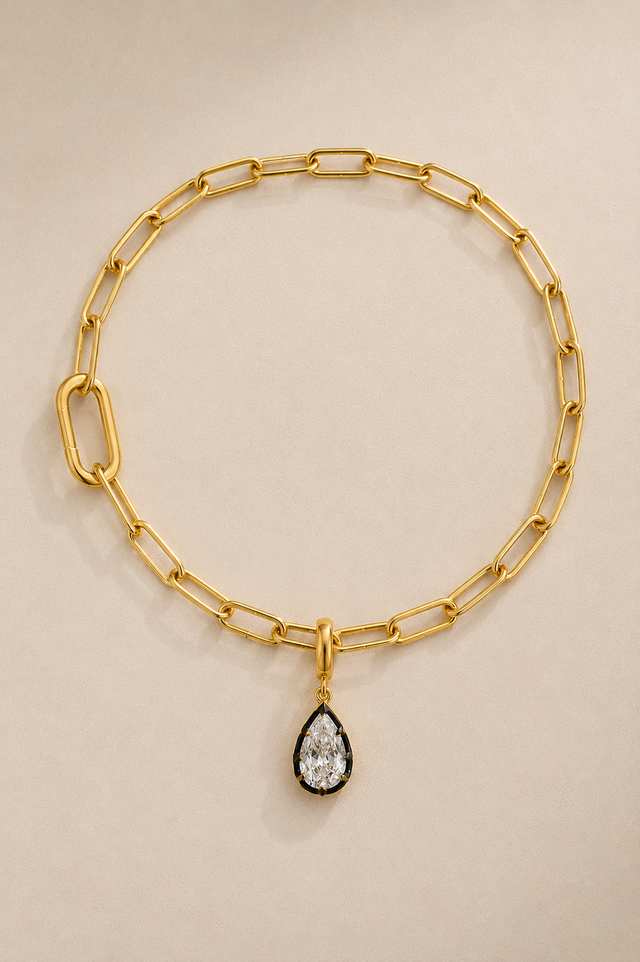 Gold paperclip bracelet with Vittoria black rhodium crystal charm on beige studio background
