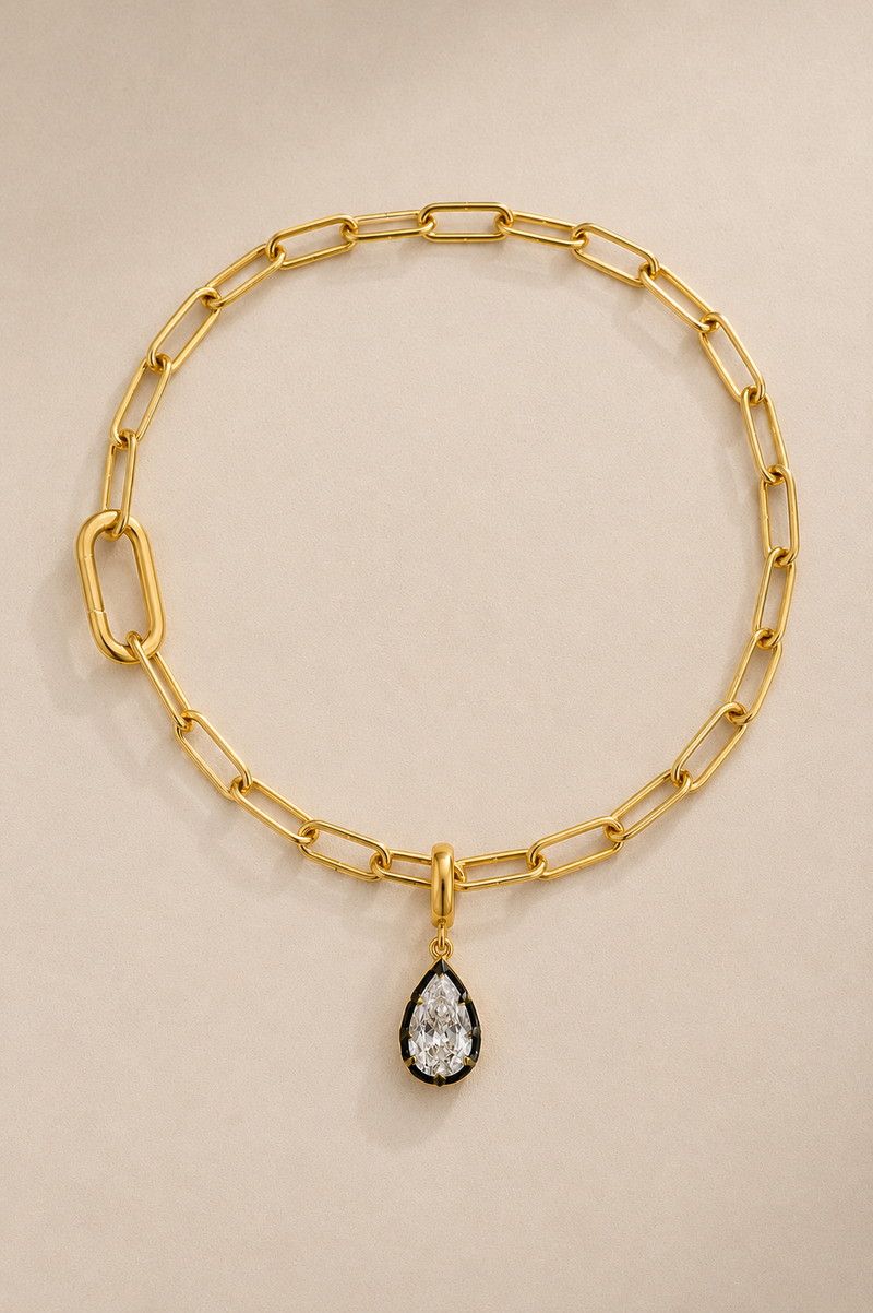 Gold paperclip bracelet with Vittoria black rhodium crystal charm on beige studio background