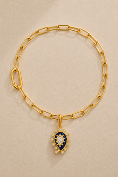 Gold paperclip bracelet with lapis paisley evil eye charm on beige background