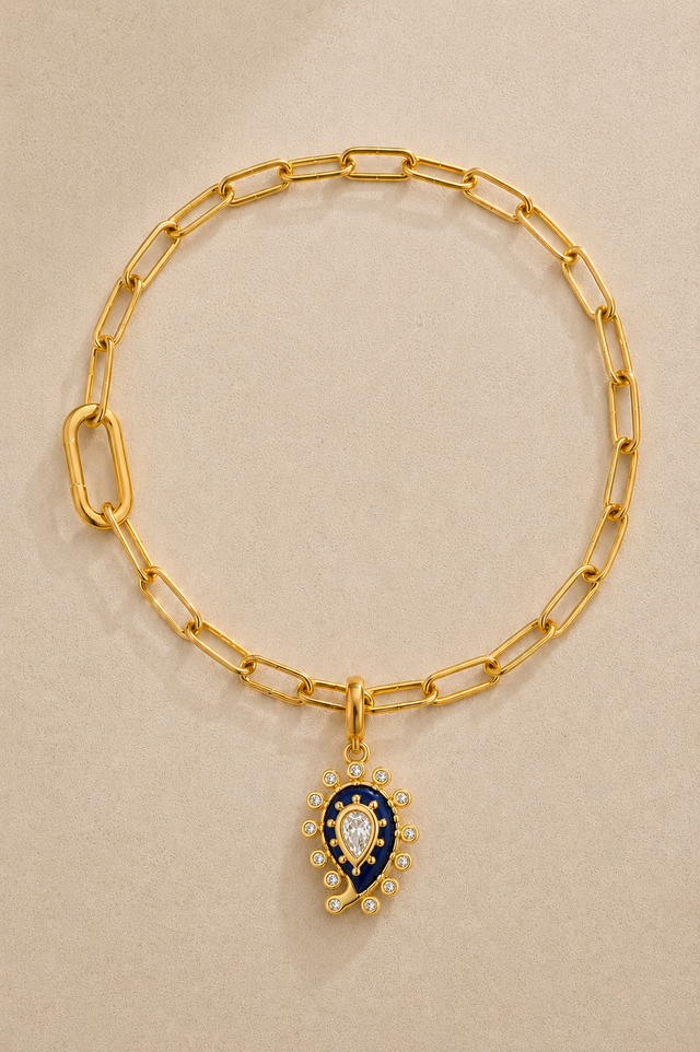 Gold paperclip bracelet with lapis paisley evil eye charm on beige background