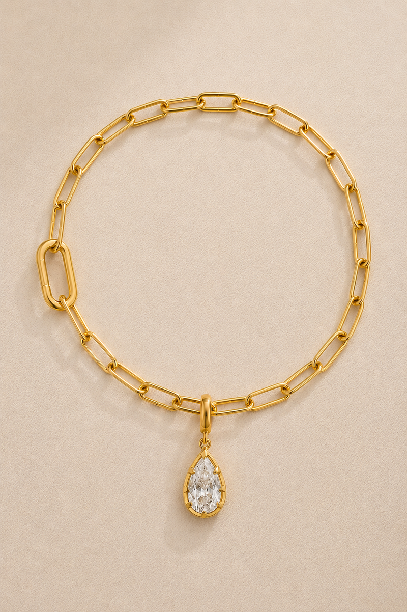 Gold paperclip bracelet with Vittoria gold crystal charm on beige studio background