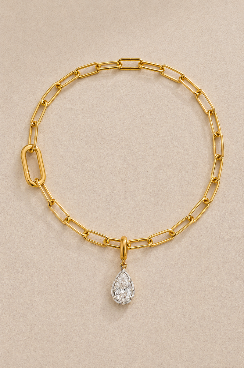 Gold paperclip bracelet with mixed-metal Vittoria crystal charm on beige studio background