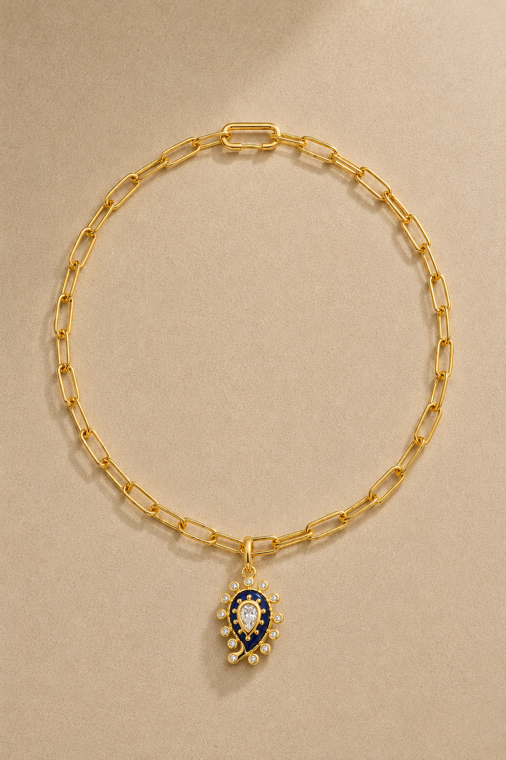 Gold paperclip chain necklace with lapis paisley evil eye charm on beige background