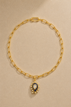 Gold paperclip chain necklace with lapis paisley evil eye charm on beige background
