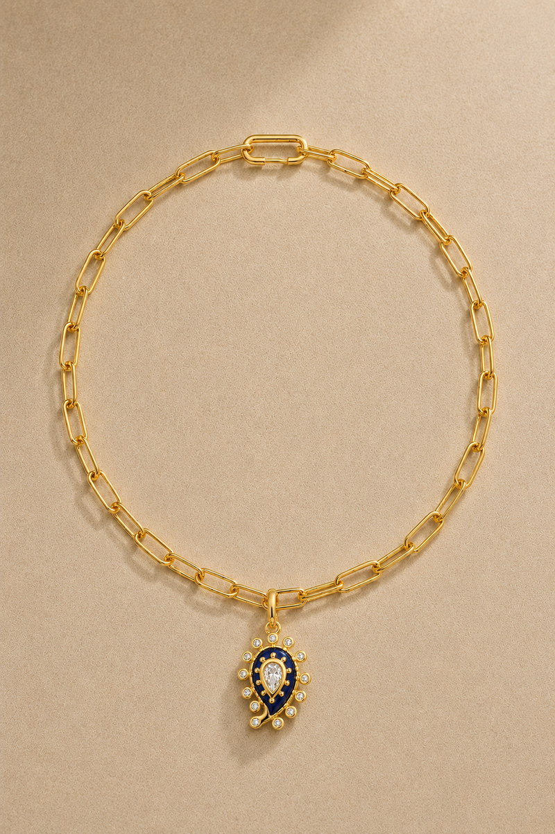 Gold paperclip chain necklace with lapis paisley evil eye charm on beige background