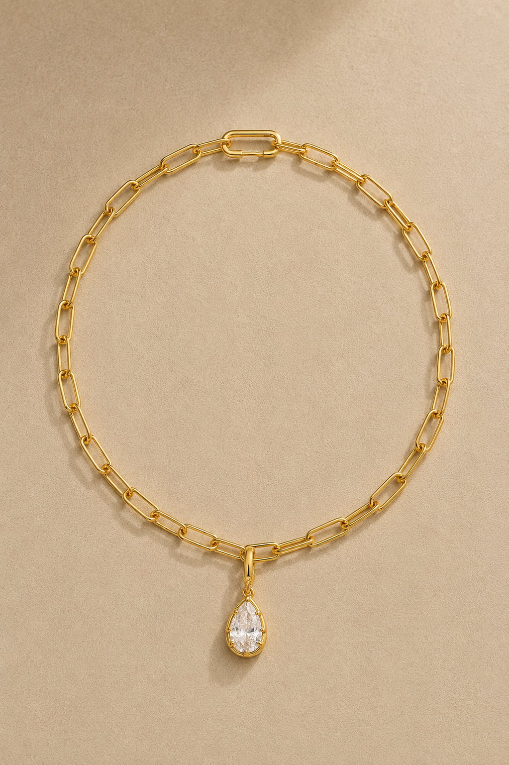 Gold paperclip chain necklace with Vittoria gold crystal charm on beige studio background